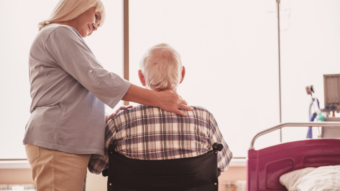 Man in wheelchair facing window with woman beside him