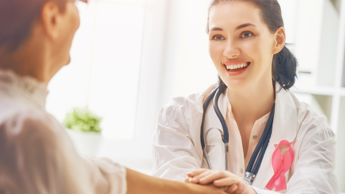 Nurse with Breast Cancer Awareness ribbon holding patient's hand