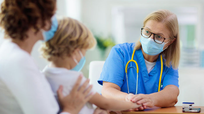 Female doctor comforting young child in mother's arms