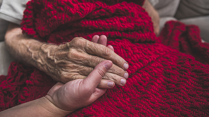 Senior hand holding younger hand on red blanket