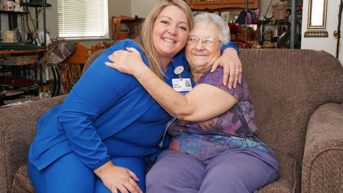 Young female nurse in blue hugging senior woman in her home
