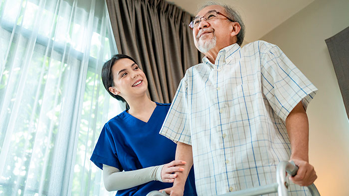 Young female nurse assisting senior man with walker in his home