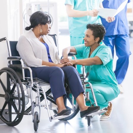Photo of female nurse kneeling and holding the hand of a female patient in a wheelchair