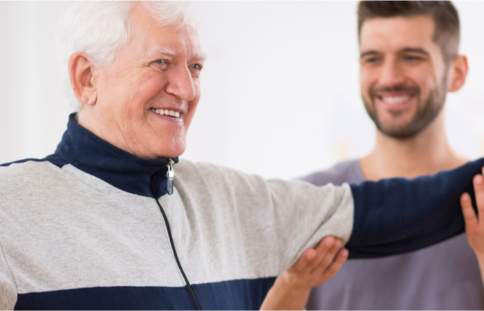 An elderly man with white hair receives treatment from a younger male therapist