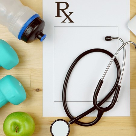 A table is covered in a prescription pad, stethoscope, water bottle, weights and an apple