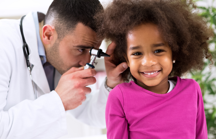 Male doctors looks in the ear of a smiling female child patient