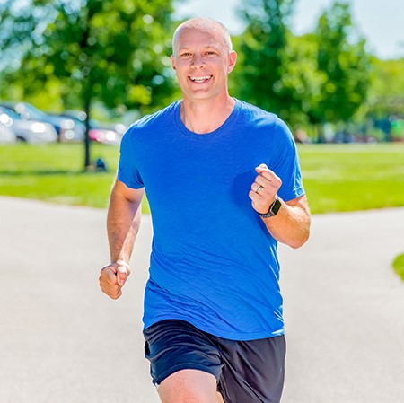 Man wearing a blue shirt jogs through the park