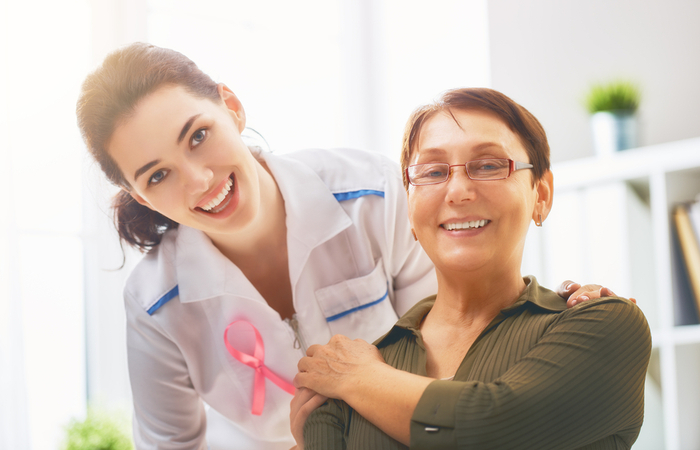 Female nurse wearing cancer ribbon stands with hand on shoulder of her patient