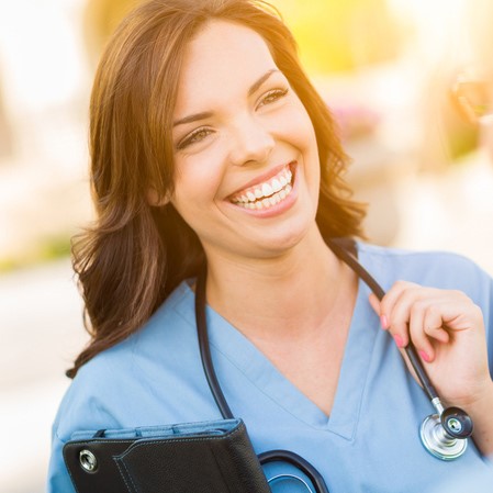 Female nurse wearing blue smiles with the sun shining on her