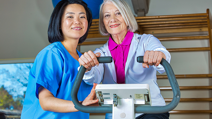 Woman on exercise equipment with nurse assisting