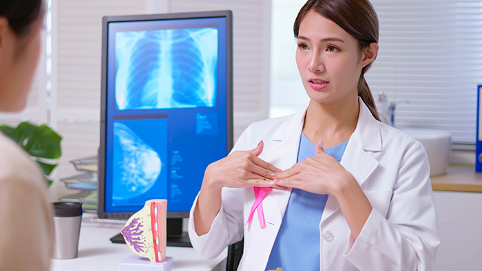 Young female doctor with pink awareness ribbon explaining breast self-exams