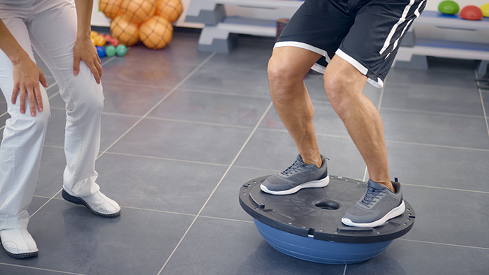 Man on balance device with physical therapist