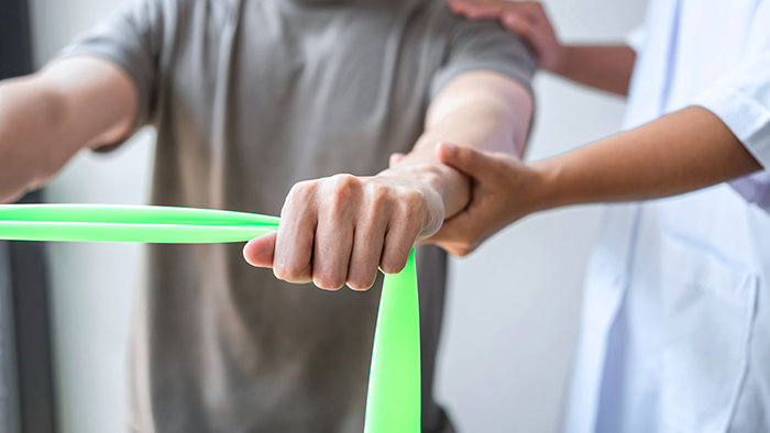 Man using a stretching band with assistance from physical therapists