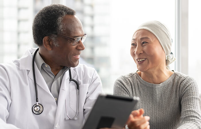 Male doctor sitting with female cancer patient wearing a head scarf.