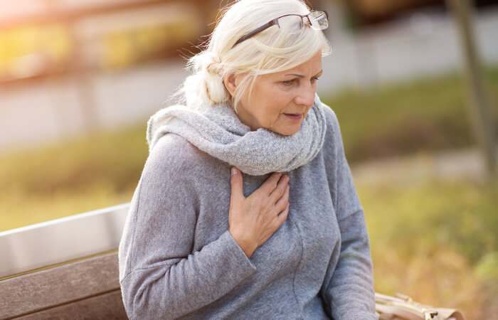Senior woman sitting outside on a park bench holding her chest as she may be having a heart attack.