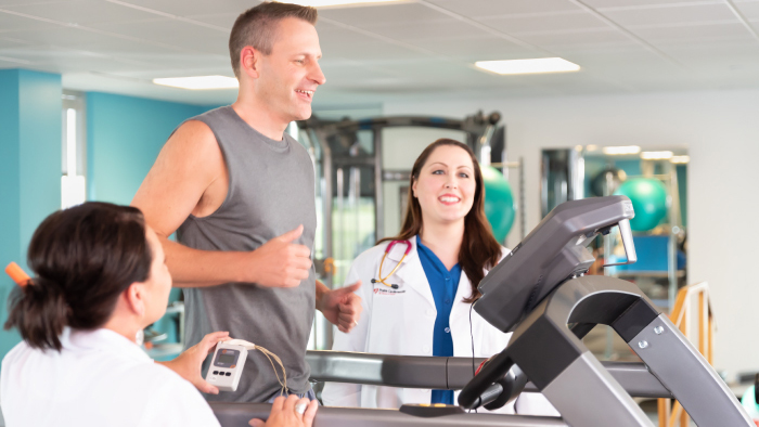 Man walking on treadmill with female physician and technician looking on