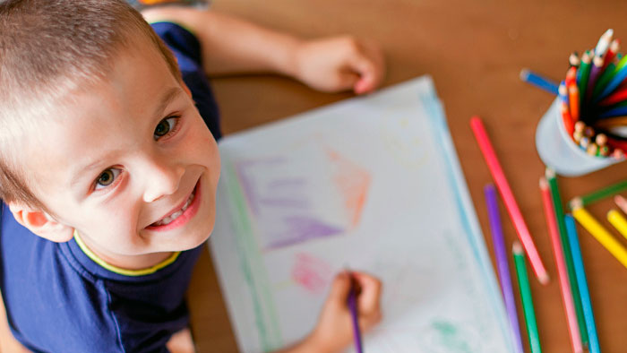 Young boy looking up from his drawing with colored pencils