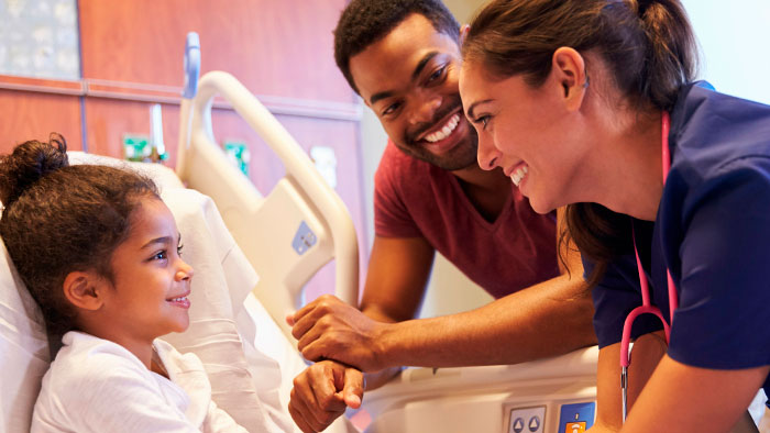 Young dad along with nurse talking with young girl in hospital bed