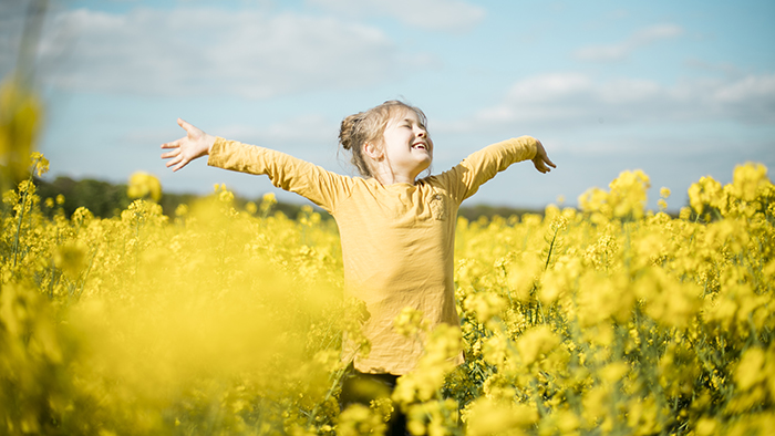 Young girl with arms stretched out in a field of yellow flowers