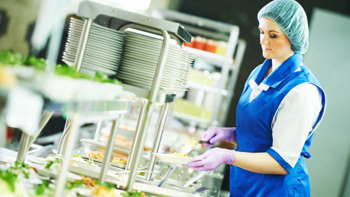 Cafeteria worker filling food trays