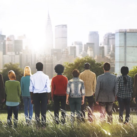 People stand in a field facing a city scape as the sun rises.