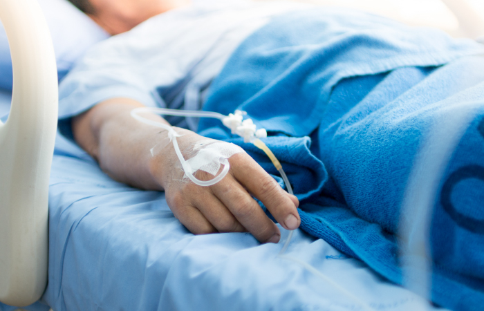 Image of patient lying in bed with IV placed in back of hand