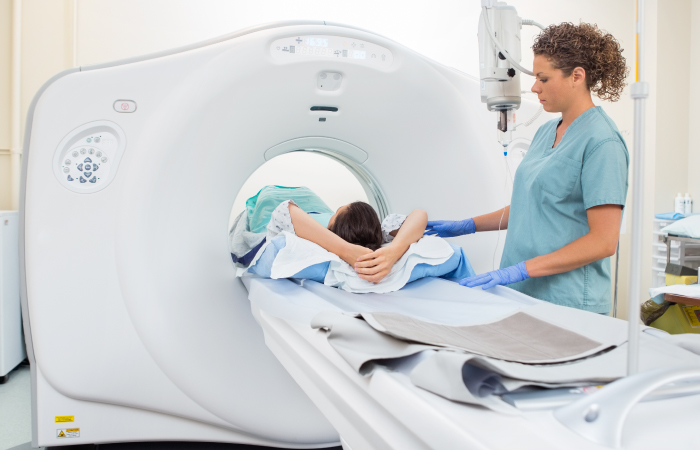 An imaging tech stand next to a patient as they slide into an MRI