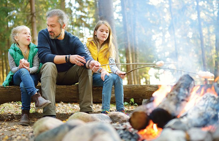 Young family in front of campfire roasting marshmellows