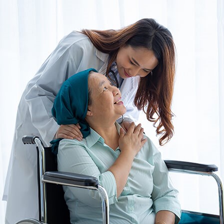 Female doctor leans down to comfort a female cancer patient in a wheel chair