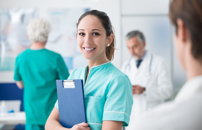 Female nurse holding patient chart against her chest, smiling looking at the camera.