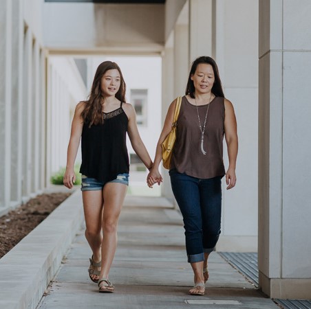 Mother and daughter walking down a sidewalk holding hands
