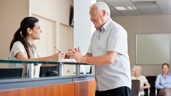 Senior man standing at reception desk talking to female receptionist