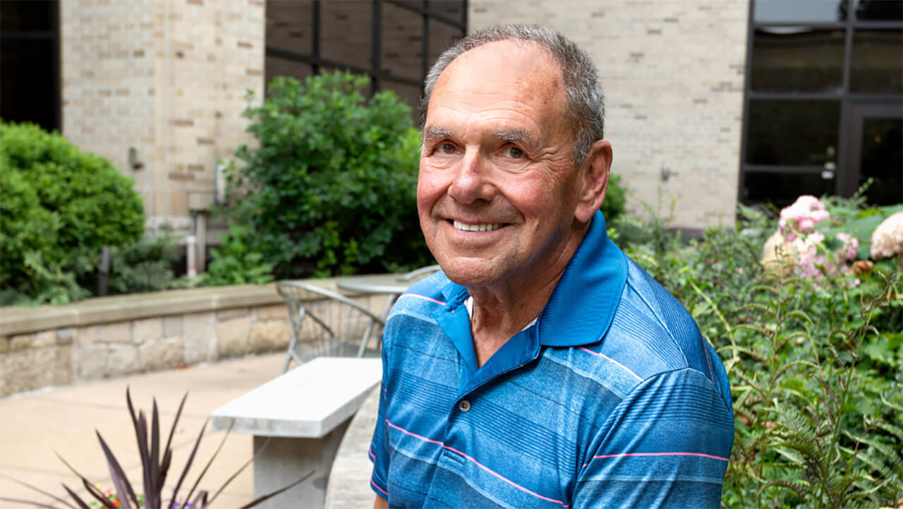 A man smiling at the camera while sitting in a garden.