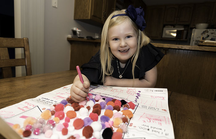 Frankie working on an art project at the kitchen table while smiling at the camera