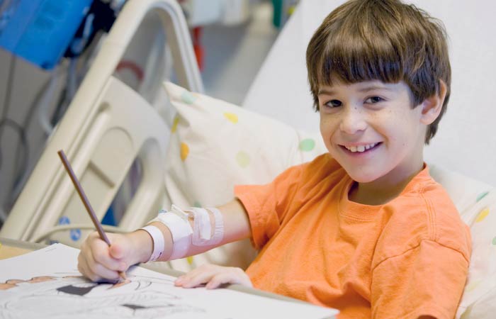 St. Vincent Children's - Young boy in an orange shirt sitting in a hospital bed with pencil and papers
