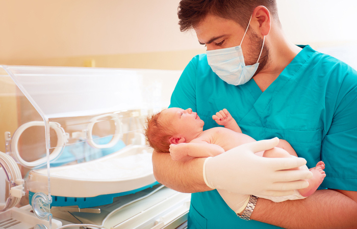 masked Male nurse holding crying infant in a hospital setting