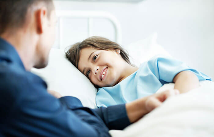 young brunette girl laying in hospital bed while adult male doctor holds her hand