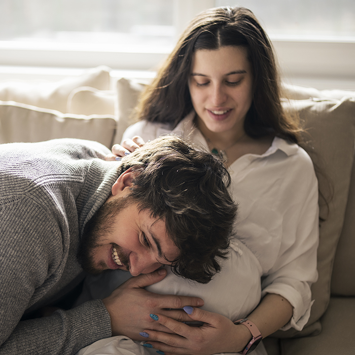 A pregnant women sits on a couch with the father listening to her belly