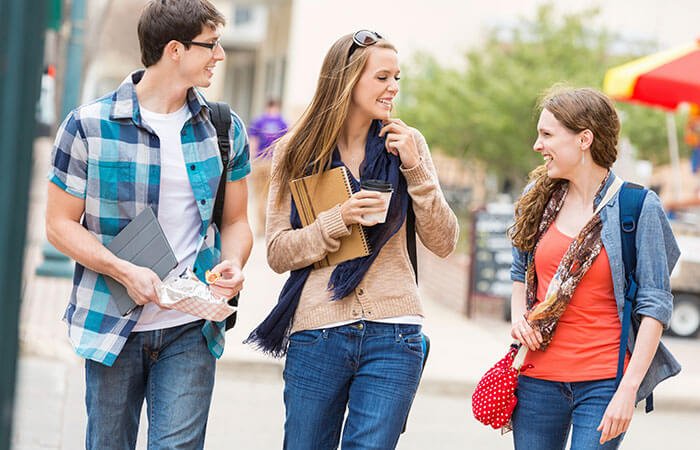 one teen boy with glasses and two teen girls with backpacks walking downtown and laughing