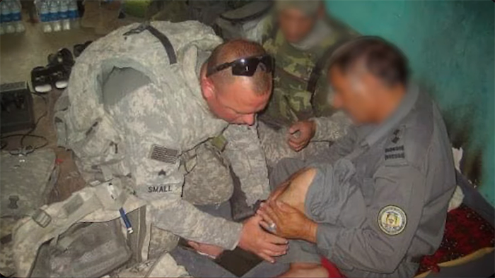 Patrick in uniform examining the shin of another veteran