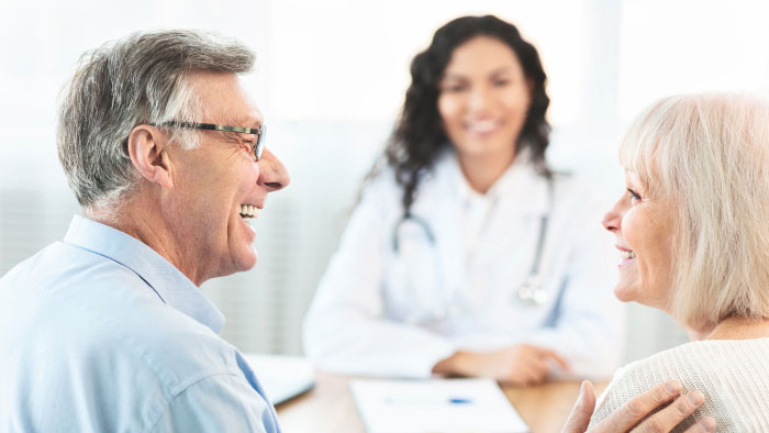 Elderly couple smiling sitting across a table from a smiling female doctor