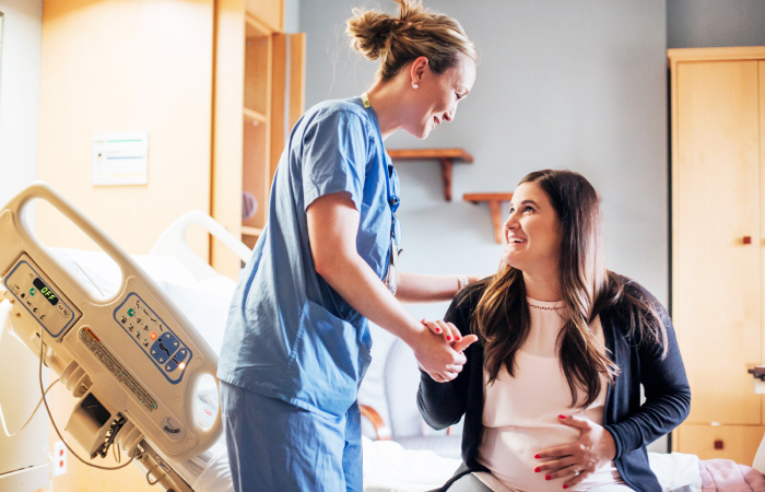 Female nurse standing over pregnant female sitting down