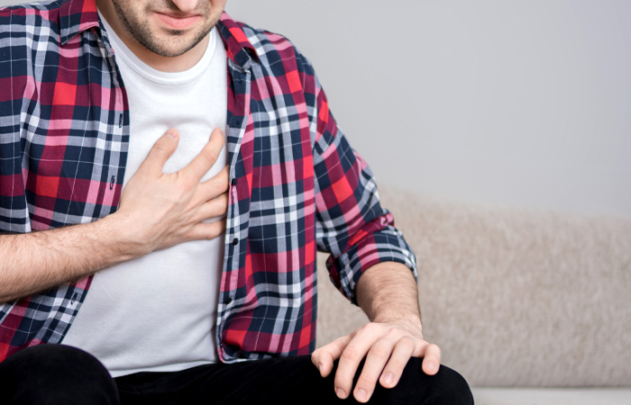 man in plaid shirt clutching his chest while seated