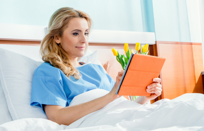 Female patient sits up in hospital bed and uses a tablet