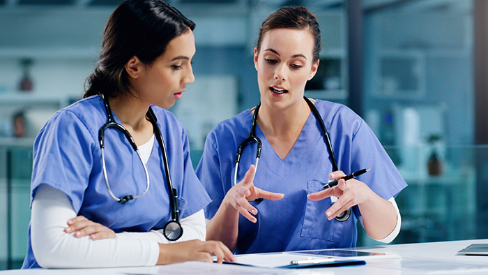 Two nurses in blue scrubs consulting over medical records