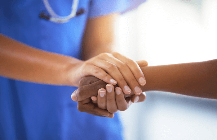 Doctor in blue holds the hand of a patient