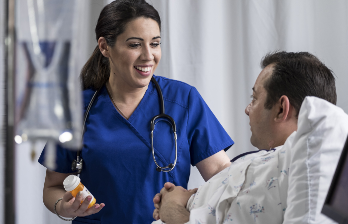 Female nurse stands beside a patient with a medication bottle in hand