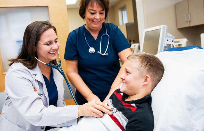 Female doctor treats a male adolescent while a female nurse stands at the bedside