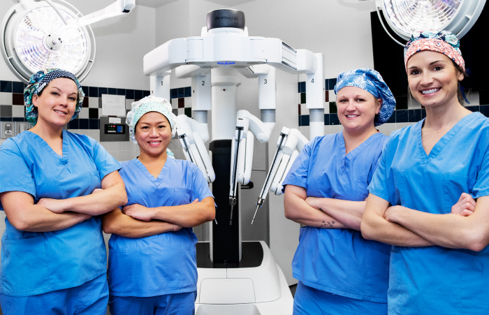 Two young and four middle aged women in scrubs standing next to surgical equipment