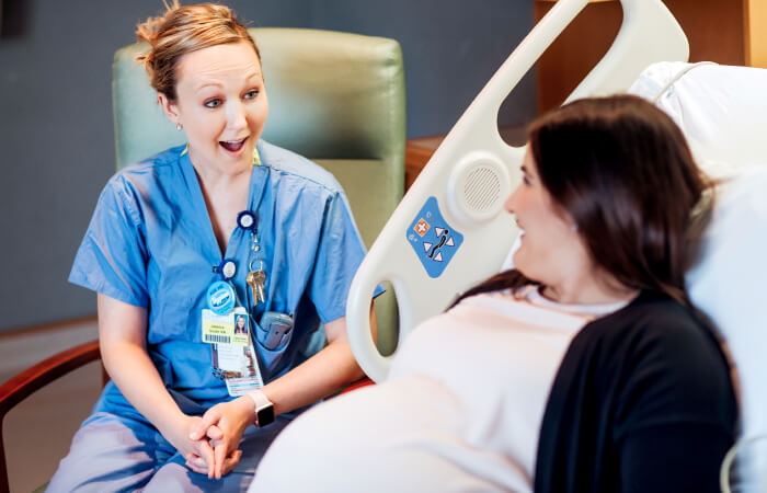 Female nurse sits at the bedside talking and smiling with pregnant mother